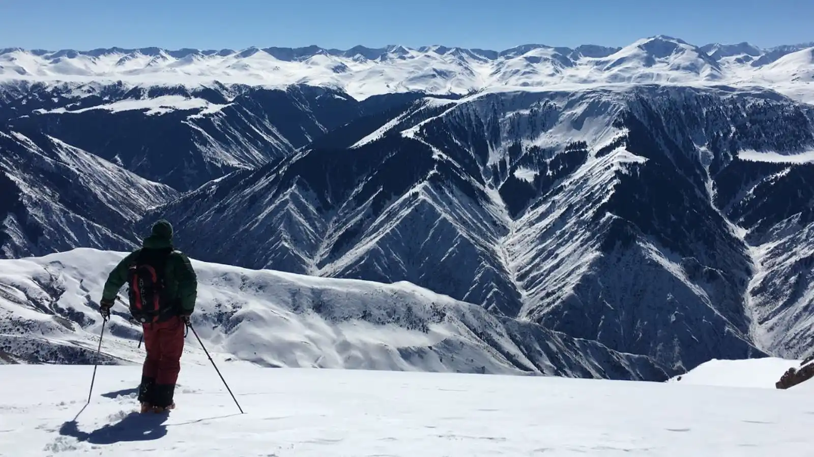 Skier with poles standing on a mountain ridge overlooking snowy peaks during a heli-ski tour